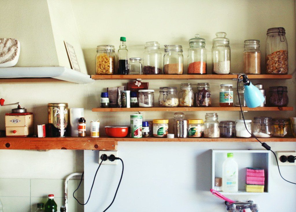 Open kitchen shelves holding glass jars of dried food and spices