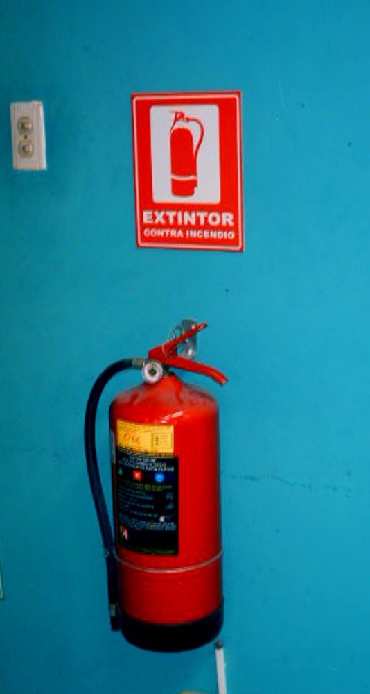 Red fire extinguisher mounted on a bright teal wall
