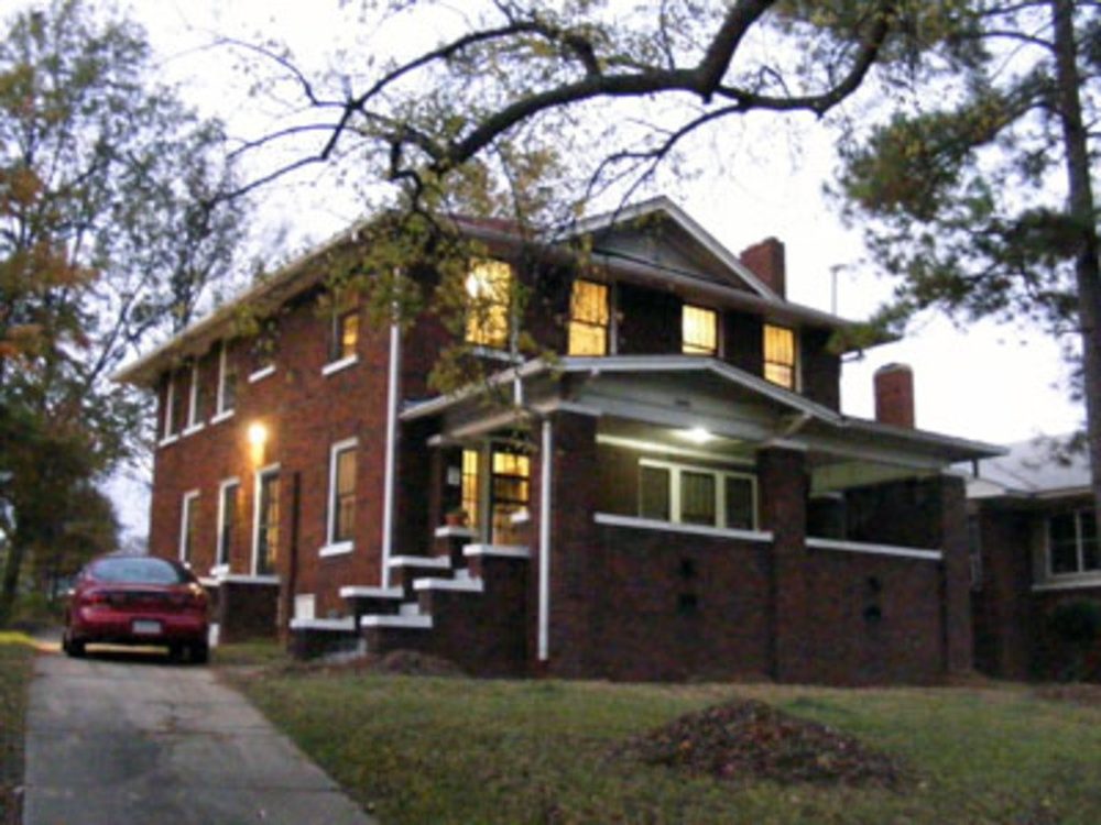 Red brick family home with a covered porch under tall trees